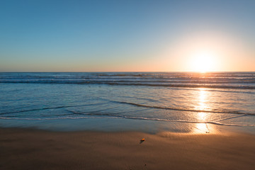 Canvas Print - Sand beach and ocean surf is painted in the colors of the setting sun. Coast of California.