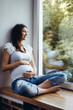 Pregnant brunette girl sitting on the windowsill