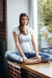 Pregnant brunette girl sitting on the windowsill