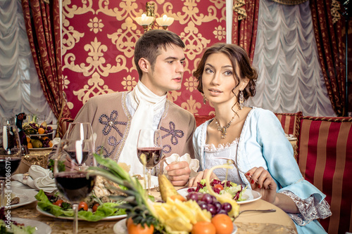 Photographie young man in a historic jacket and girl in vintage dress sitting at the richly laid table in a restaurant