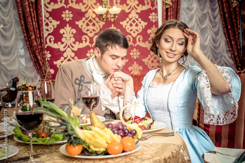 young man in a historic jacket and girl in vintage dress sitting at the richly laid table in a restaurant Poster