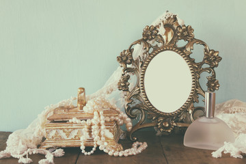 Antique blank victorian style frame, perfume bottle and white pearls on wooden table. retro filtered and toned. template, ready to put photography
