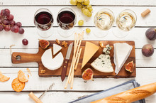 Red And White Wine Plus Different Kinds Of Cheeses (cheeseboard) On Rustic Wooden Table. French Food Tasting Party Or Feast Scenery From Above (top View).