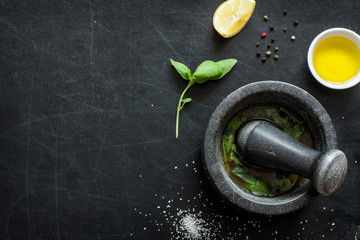 Basil vinaigrette dressing - recipe ingredients on black chalkboard background from above. Fresh basil leaves, lemon, olive oil, salt, pepper and mortar. Layout with free text space.