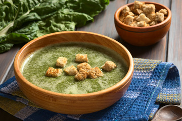 Poster - Cream of chard soup with croutons in wooden bowl, photographed on dark wood with natural light (Selective Focus, Focus on the first croutons)