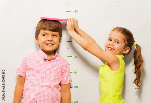 Fotografía Boy and girl measure height by wall scale at home