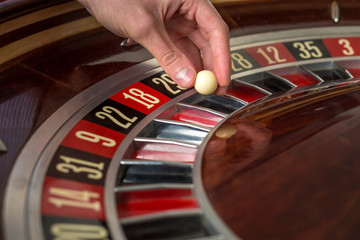 Roulette wheel and croupier hand with white ball in casino 