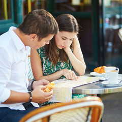 Wall Mural - Young romantic couple using map in a cozy outdoor cafe in Paris, France