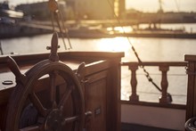 Steering Wheel Of An Old Wooden Sailing Ship In A Port At Sunset