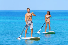 Man And Woman Stand Up Paddleboarding On Ocean. Young Couple Are Doing Watersport On Sea. Male And Female Tourists Are In Swimwear During Summer Vacation.