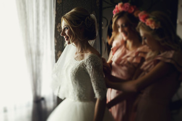 Bridesmaids in pink preparing beautiful elegant white dress brid