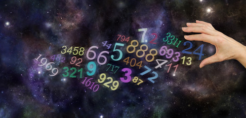 The Universal Significance of Numbers - female hand about to take number 24 amongst a group of scattered multicolored transparent numbers on a wide deep space background with copy space
