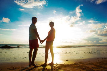 Wall Mural - sunset silhouette of young couple in love holding hands at beach