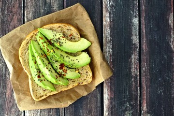 Wall Mural - Open avocado sandwich with whole grain bread on paper against a rustic wooden background
