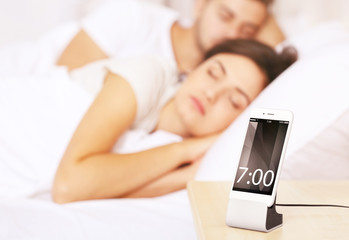 Wall Mural - Happy couple waking up with mobile alarm clock