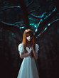 The little red-haired girl in a white dress walks in the mystical and mysterious forest.Princess with a crown standing near the tree,creative computer colors,fashionable toning