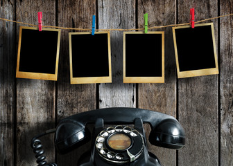 Old picture frame hanging on clothesline and old telephone on wood background.