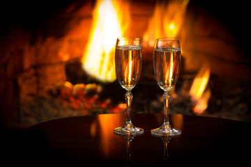 two glasses of sparkling white wine in front of warm fireplace. romantic, cozy relaxed magical atmos