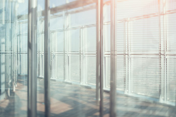 Abstract office interior background, the sun rays with flares, glass, steel columns and blinds, view from skyscraper through the window, the cityscape outside