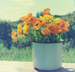 Yellow summer flowers in an iron white mug . Bouquet from a marigold. Calendula flowers. Festive bouquet in vintage style