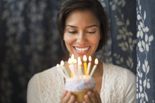 Woman Looking Down At Lit Candles On Birthday Cupcake