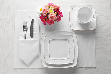 Wall Mural - Table setting with dishes, cutlery and flowers on white background