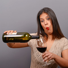 Portrait of woman holding wine bottle and glass against gray bac