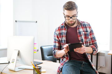 Poster - Concentrated man sitting on table in office and using tablet