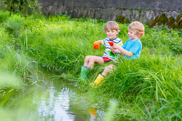 Wall Mural - Two little brothers playing with paper boats by a river