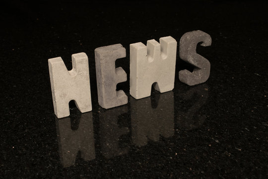 Word News as grey concrete letters on black tile