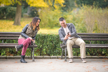 Wall Mural - Two young people sitting on benches in a park and exchanging phone numbers