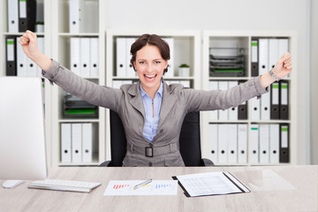 Successful Businesswoman With Arms Outstretched At Desk