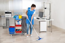 Happy Female Janitor Mopping Floor In Office