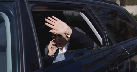 Wall Mural - Annoyed female business woman on phone in back of car with window down trying to block the view with hand near face