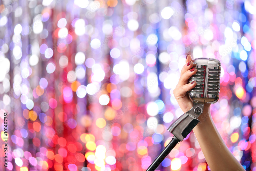 Female hands holding microphone against bright glitter background