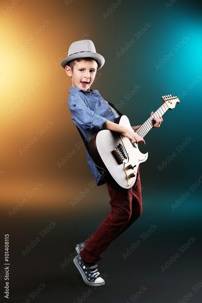 Little boy playing guitar on a dark lighted background