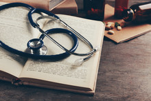 Book, Pills And Stethoscope On Wooden Table Closeup