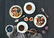 Healthy breakfast set. Bowls of oat granola with yogurt, fresh blueberries and figs, coffee, honey, over black wooden backdrop