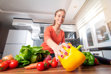 Wall Mural - Wide angle view of young woman holding yellow pepper cooking in new kitchen making healthy food with vegetables. Focus on the sweet pepper.