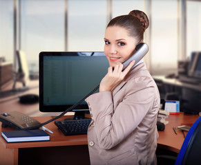 Young businesswoman sitting at desk and working. Smiling and looking back at camera