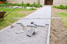 Bricklayer Places Concrete Paving Stone Blocks For Building Up A Patio, Using Hammer And Spirit Level