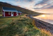 Red Cottage Seaside With Plant Foreground And Mountain Range Background During Sunrise Time At Eskifjorour Iceland In Autumn Season
