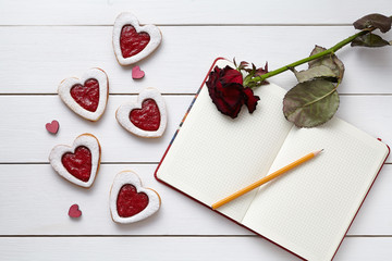 Wall Mural - Heart shaped cookies with empty notebook, pencil and red rose gift on white wooden background. 