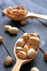 Wall Mural - Spoons with walnuts, pistachios and peanuts, on grey wooden background