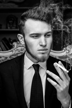 Close Up Portrait With Casual Young Man Sitting In Vintage Chair With A Cigarette. Black And White Photo