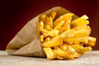 French fries in the paper bag on burned background on wooden table