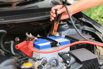 Car mechanic uses battery jumper cables charge a dead battery.