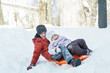 © nkarol - Sibling children laughing and riding downhill on winter orange toboggan sledge made of plastic outdoor