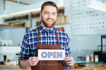 Sticker - Happy attactive young barista holding open sign at coffee shop