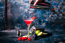 Barman Preparing And Pouring Red Cocktail In Marini Class. Cosmopolitan Cocktail On Metal Background